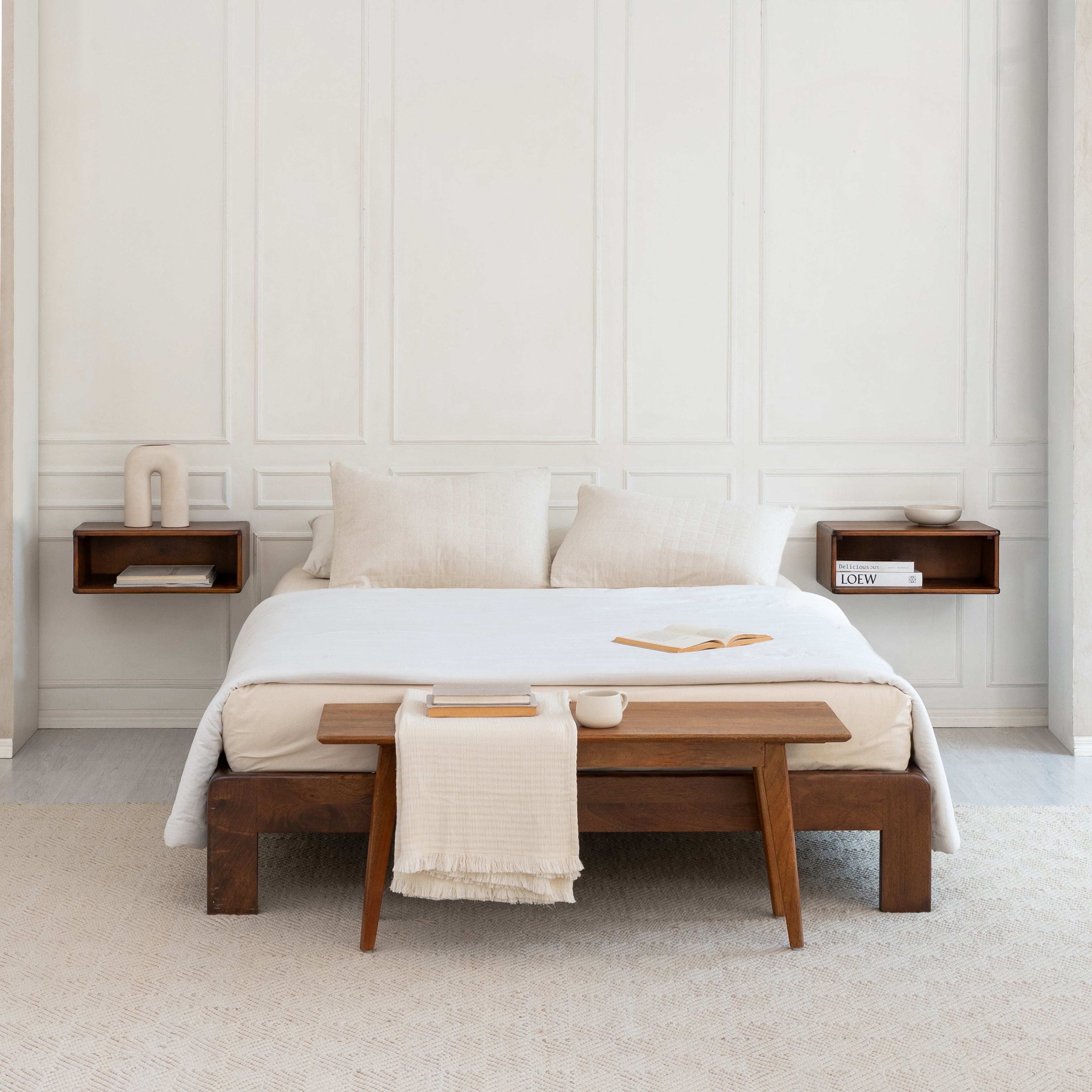 Modern bedroom with a bed, wooden bench, and bedside tables against a white paneled wall.